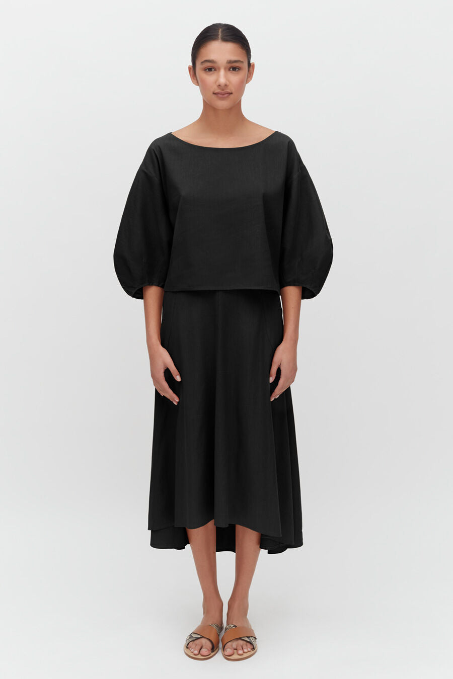 Woman in a blouse and skirt standing straight, facing forward.