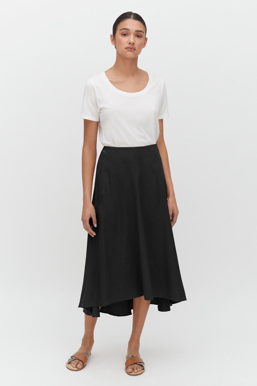 Woman in a T-shirt and mid-length skirt standing straight with sandals.