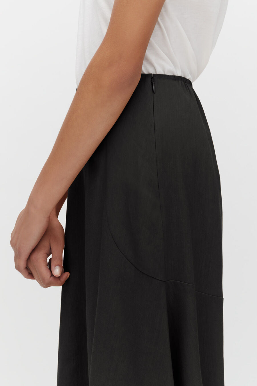 Person standing with hand on hip, wearing a skirt and T-shirt.