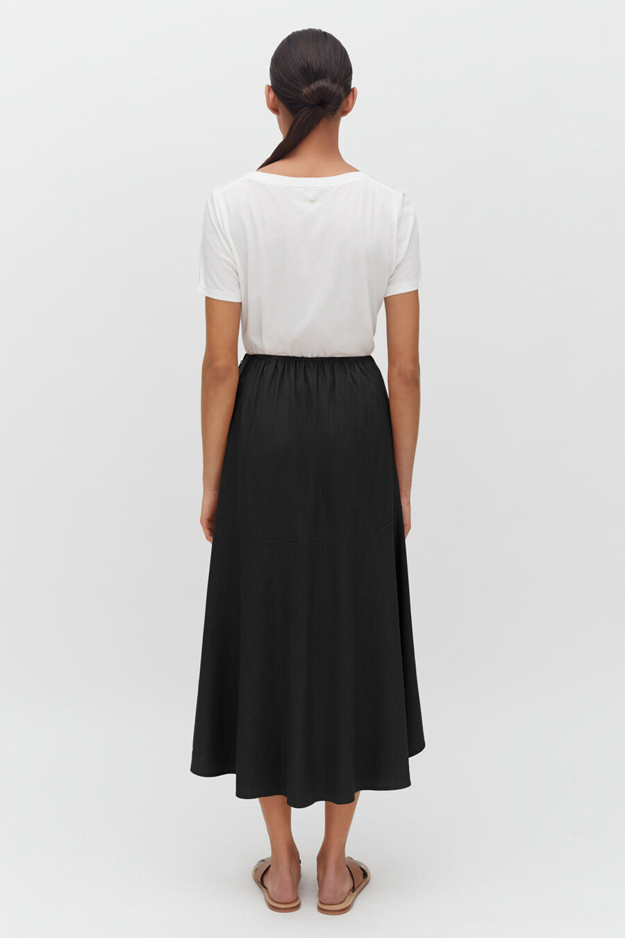 Woman facing away, wearing a top and a long skirt, standing upright.