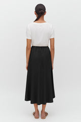 Woman facing away, wearing a top and a long skirt, standing upright.